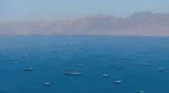 Множество судов на сравнительно небольшом участке моря, вид с дрона. На заднем плане горы