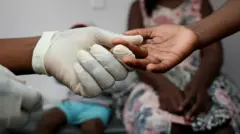 Aworan ọwọ nọọsi to fẹẹ ṣe ayẹwo ẹjẹ fun ọmọde kan.