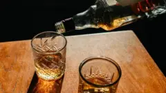 Masa üzerinde iki içki kadehi, birine şişeden içki boşaltılıyor