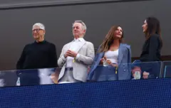 Bill Gates e outras três pessoas do alto de um camarote vendo o jogo no estádio
