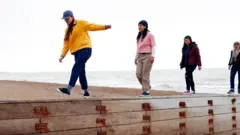 Pessoas andando sobre uma mureta na praia