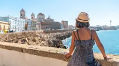 Młoda turystka w słomkowym kapeluszu i kwiecistej sukience spoglądająca na wybrzeże Kadyksu oraz katedrę w Andaluzji.