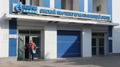 мужчина в спецодежде выходит из здания, на котором большими буквами написано "газпромнефть", омский нефтеперерабатывающий завод 