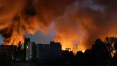 A skyline shot of Kyiv shows plumes of smoke and flames rising over buildings.
