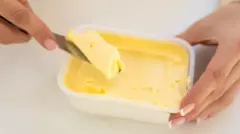 Duas mãos seguram um pote de margarina para retirar parte do produto com uma faca