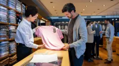 Vendedora mostra camiseta para comprador em loja de roupas