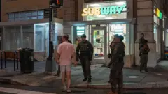 Há um grupo de agentes uniformizados em pé do lado de fora de uma lanchonete Subway.