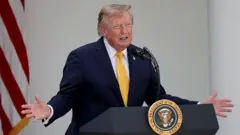 President Donald Trump speaks during an event in the Rose Garden of the White House. He is animating with his hands and is wearing a suit with a yellow golden tie. 
