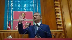 Özel Meclis kürsüsünde sağ elini kaldırmış konuşuyor. 