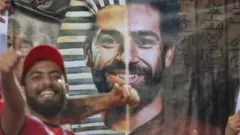 Seorang warga Mesir berfoto di depan spanduk pemain Liverpool, Mohamed Salah.