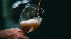 Hand hold one glass cup and beer dey pour inside