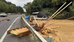 川にかかる道路上に、流されてきた木製の階段や木材などが残されている。川の水は茶色く濁り、水位が道路の高さまで迫っている