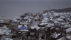 İsrail saldırıları nedeniyle yerlerinden edilen Filistinliler, 15 Aralık 2025'te Gazze şehrinde derme çatma çadırlarda hayatta kalma mücadelesi veriyor. Kapalı havada onlarca derme çatma çadır, ileride deniz görünüyor. 