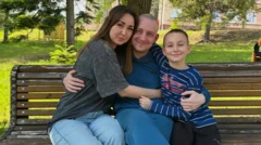 Vestindo um moletom azul e calças azuis, o major Oleksandr Ivanov está sentado em um banco de parque entre a sua mulher, Nelly, de camiseta cinza-escura e jeans, e o filho, Demid, de camiseta listrada azul com letras vermelhas e calças pretas. Os três sorriem e se abraçam