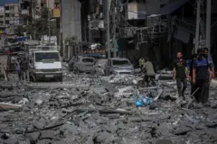 A street in the Rimal neighbourhood of Gaza City is littered with rubble. Many destroyed cars can be seen lining the streets as peole congregate in small groups