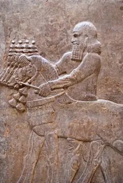 Figura de um homem esculpida na pedra, de corpo inteiro, de perfil com um cavalo e outros cavalos ao fundo