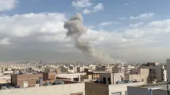 Міський краєвид із пласкими дахами та щільною забудовою пісочного кольору будівель. На горизонті простягається гірський хребет, а з району вдалині здіймається великий стовп густого сірого диму.