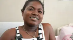 Andreína Sarmiento smiles as she looks into the camera while sitting next to a hospital bed.