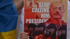 Справа женская рука держит рисунок, на котором Лукашенко и спецназ на фоне надписи по-английски "Прекратите называть его президентом", а слева кто-то с флагом Украины