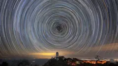 Una foto nocturna del cielo que muestra rastros de estrellas formando una espiral sobre el Telescopio Mayall que alberga DESI.