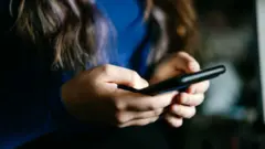 Bir çocuk elinde bir telefon tutuyor. 