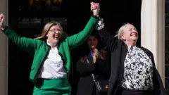 Two women hold hands in the air in celebration in a doorway