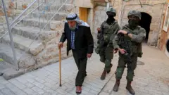 شيخ فلسطيني وخلفه جنديان إسرائليليان بمدينة الخليل بالضفة الغربية المحتلة 