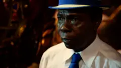 Paulinho da Costa usando uma gravata e um chapéu azul