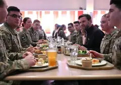 Casal Vance almoçando com militares; todos estão em mesa, comendo pratos em bandejas
