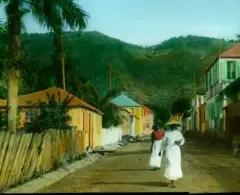 Dos personas con falda y sombrero caminan por una calle de St. Thomas, en las Islas Vírgenes de EE.UU., en una imagen de alrededor de 1890.