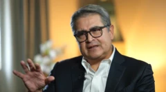 El expresidente de Honduras, Juan Orlando Hernández, vestido con una americana oscura y camisa blanca con el primer botón suelto, mira al entrevistador, de espaldas a un fondo desenfocado.