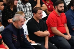 Lula sentando em um evento ao lado dos filhos