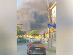 黒い車が走る道の向こう、建物の上に大きい黒煙が立ち上っている