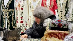 Бозорда ўзбек миллий дўппи ва кийим-кечакларини сотаётган аёл.