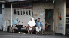 Munikah sedang berjaga di depan warungnya yang menjual kebutuhan pokok.