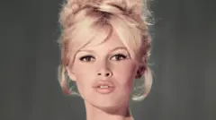 Portret studyjny Brigitte Bardot w jasnoniebieskiej sukience z odkrytymi ramionami, z blond fryzurą w kształcie ula i lekko rozchylonymi ustami.