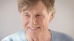 On voit Robert Redford dans ses vieux jours. Il sourit et regarde légèrement hors champ.