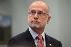 El presidente de la FCC, Brendan Carr, vestido de traje oscuro y corbata roja con diseños, mira de lado.
