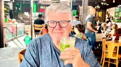 William sentado em bar, mostrando copo de caipirinha
