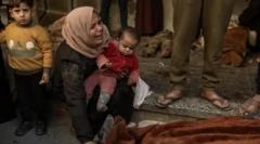أم تمسك بطفلها وهي تبكي، بينما يقف طفل صغير في الخلفية