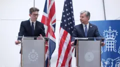 Umukuru wa MI5  Ken McCallum (i bubamfu) n'uwa FBI  Christopher Wray (i buryo) baremeshereje hamwe ikiganiro n’abanyamakuru, ibitari bwigere bibaho, i Londres