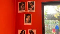 La imagen muestra cinco fotografías en blanco y negro de mujeres identificadas que fueron secuestradas durante el régimen de Pinochet y torturadas en el centro de detención. Las fotografías, que rinden homenaje a estas mujeres, están colgadas en una pared de color rojo vivo en el interior del memorial.