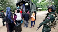 Люди из разных стран, работавшие на территории комплекса KK Park в Мьянме, перебрались в Таиланд через реку Моэй и садятся в автомобиль, пока тайские солдаты несут дежурство в округе Мэсот, провинция Так, 24 октября 2025 года