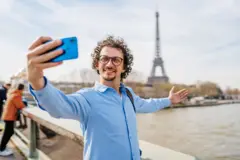 Homem tirando selfies com seu smartphone em uma ponte em Paris, na França. Vista da Torre Eiffel ao fundo.