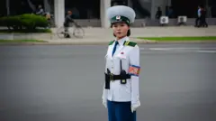Pyongyang'da bir meydanda beyaz üniformalı bir kadın var. Trafik polisi olduğu anlaşılıyor. Direkt olarak kameraya bakarak gülmeden poz veriyor.