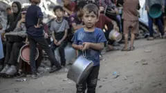 Uma criança com uma panela enorme na mão na esperança de coletar comida para si e sua família