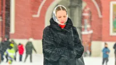 Женщина в черном пальто и белом платке, перед ней виден снег