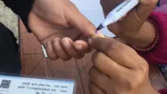 मतदान गरेको सङ्केतस्वरूप एक मतदाताको औँलामा मसी लगाइदिँदै एक कर्मचारी