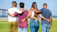 Quatro jovens abraçados de costas de frente para uma baía