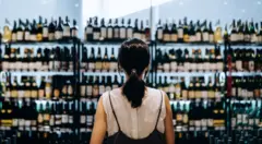 Vista traseira de uma jovem comprando vinhos em um supermercado. Ela está em frente à seção de bebidas alcoólicas